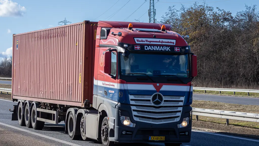 A tractor unit hauling a forty-foot shipping container on a skeletal chassis along a main road.