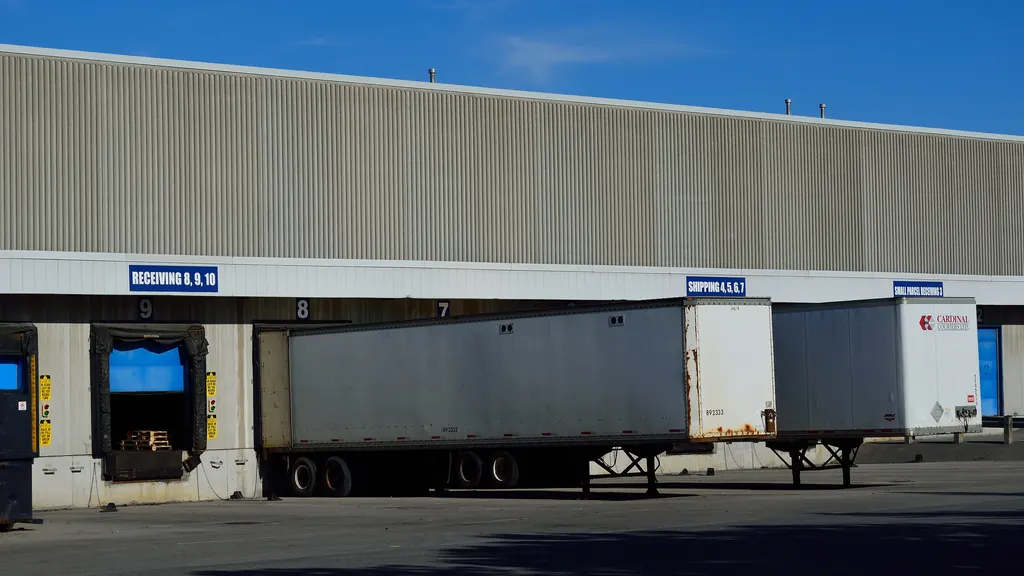 Semi-trailers backed onto numbered loading bays along a warehouse wall, with the doors signed for shipping and receiving and pallets visible inside one open bay.