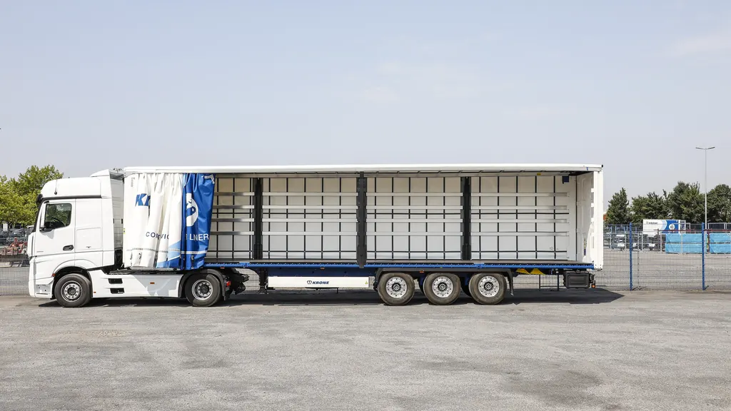 A curtainsider semi-trailer with the curtain drawn fully back along one side, showing the empty deck and the load-restraint battens down its length.