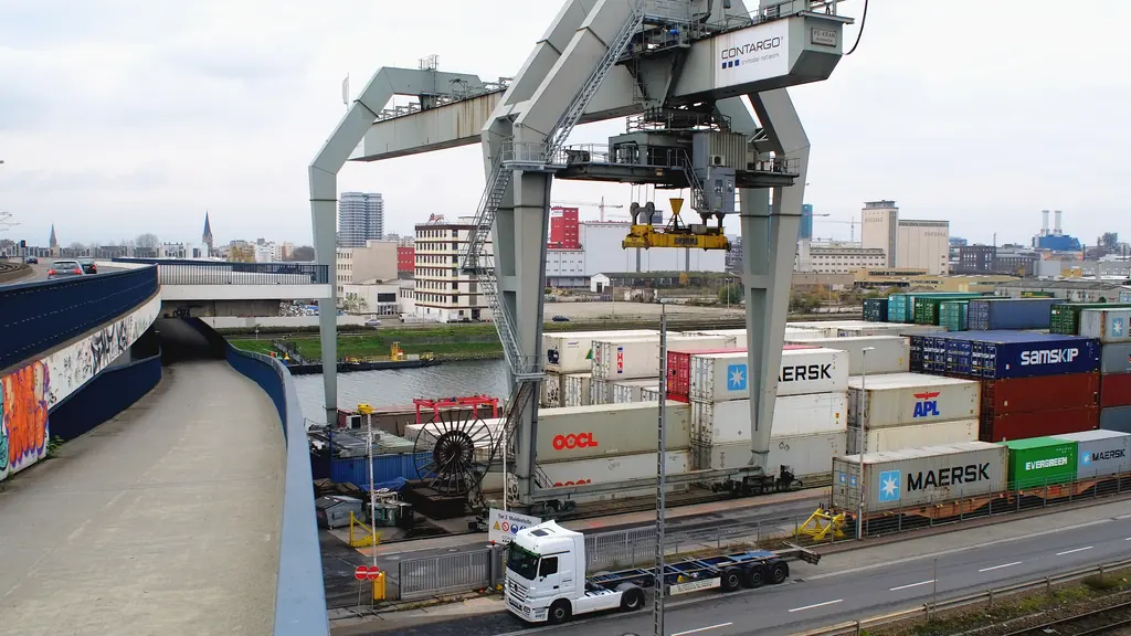 A rail-mounted gantry crane over stacked containers at an inland terminal, with a road running alongside.
