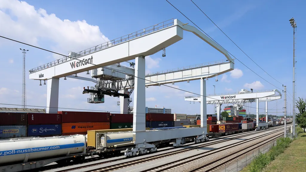 Rail-mounted gantry cranes spanning loaded container wagons at an inland terminal, with a road running alongside the tracks.