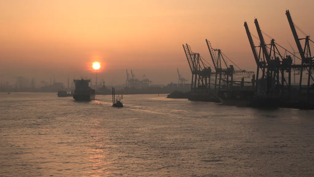 Container cranes silhouetted along a harbour skyline at daybreak, with a vessel under way.