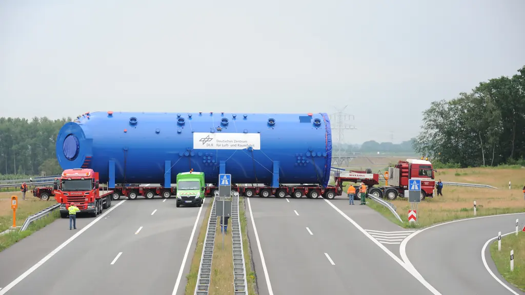 An abnormal load — a large cylindrical vessel on a multi-axle trailer — moving along a closed motorway with escort vehicles.