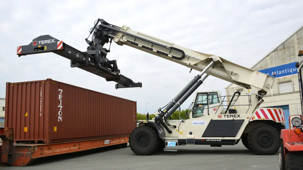 A reach stacker lifting a shipping container by its top corner castings at a port.