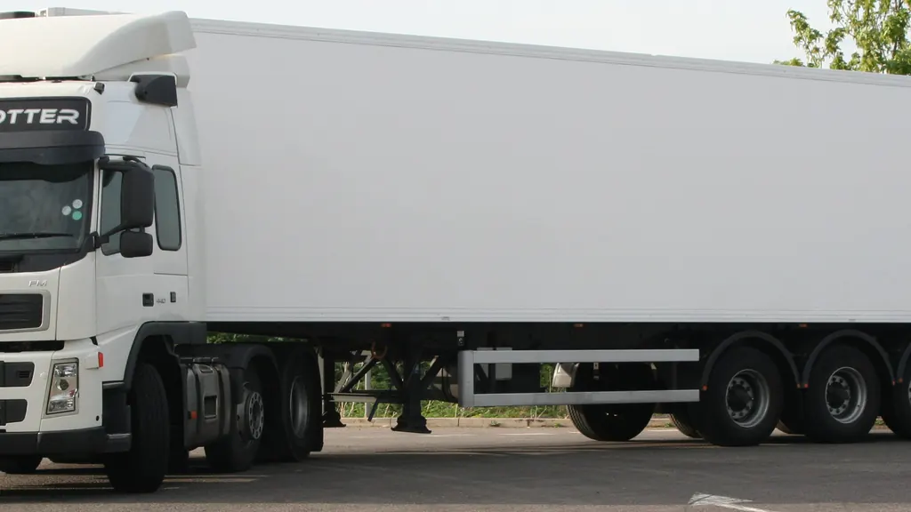A tractor unit coupled to an unmarked refrigerated box semi-trailer, standing on a hard surface in daylight.