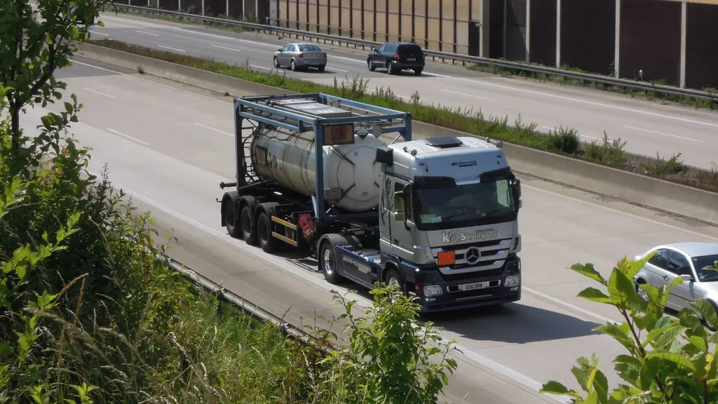 An articulated lorry carrying a tank container on a motorway, seen from an overbridge.